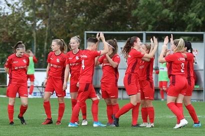 Gruppe von Frauen in roten Fu&szlig;balltrikots feiert gemeinsam auf einem gr&uuml;nen Rasenplatz.