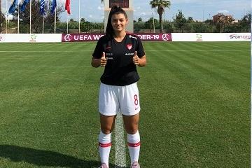 Fu&szlig;ballspielerin mit Daumen hoch, steht auf dem Rasen eines Sportfeldes, Hintergrund mit Flaggen und Stadionanzeige.