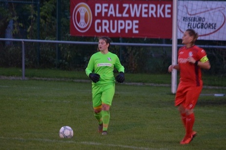 Fu&szlig;ballspiel mit einer Torh&uuml;terin in gr&uuml;ner Uniform und einer Spielerin in roter Kleidung auf dem Spielfeld.