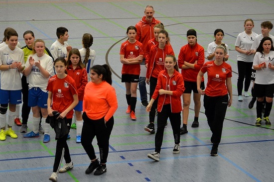 Gruppenszene mit jungen Fu&szlig;ballspielerinnen in Sportkleidung, die sich in einer Halle versammeln.