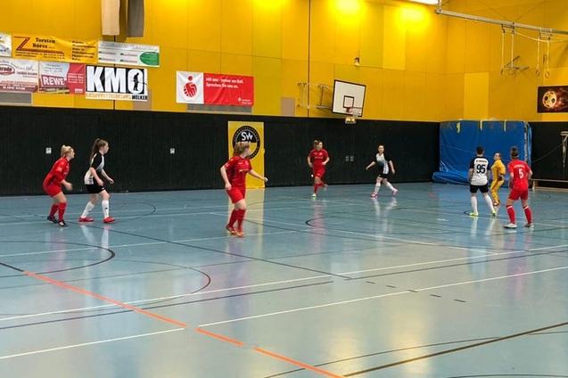 M&auml;dchenfu&szlig;ballspiel in einer Halle, zwei Teams in roten und schwarzen Trikots stehen sich auf dem Spielfeld gegen&uuml;ber.