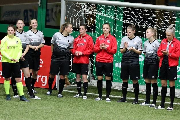 Mannschaft von Frauenfußballspielern steht in Uniformen an einem Fußballtor und applaudiere während einer Veranstaltung.