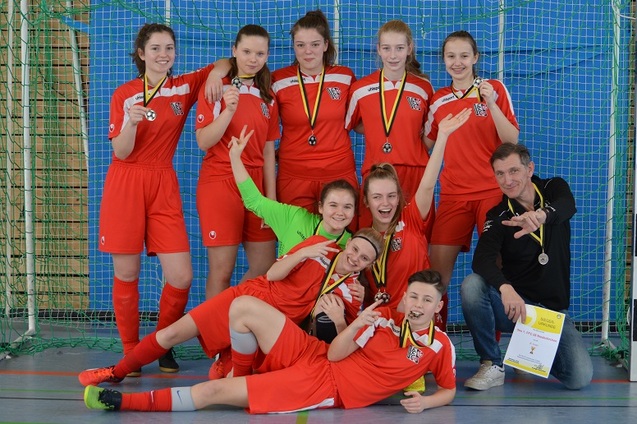 Gruppe von neun Fu&szlig;ballspielerinnen in roten Trikots mit Medaillen, posierend auf einem Sportfeld.