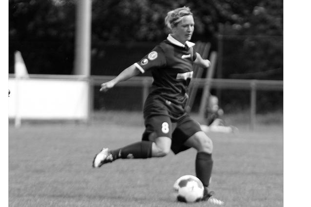 Spielerin in schwarzem Trikot schie&szlig;t auf einem Fu&szlig;ballplatz einen Ball mit Pr&auml;zision.