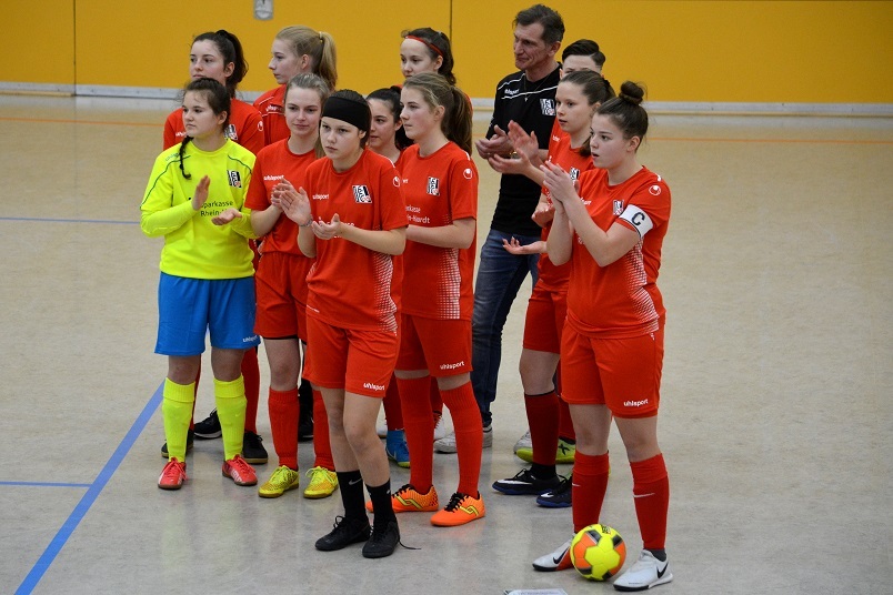 Mannschaft von Fu&szlig;ballspielerinnen in roten Trikots und einem Torwart in Gelb applaudiert in einer Halle.