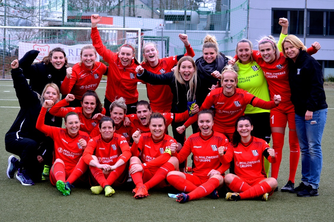 Frauenfu&szlig;ballmannschaft in roten Trikots posiert jubelnd auf dem Platz, umgeben von Stolz und Freude.