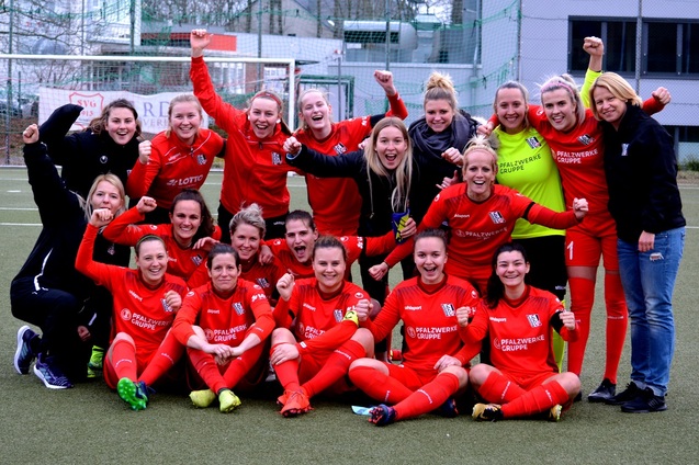 Frauenfu&szlig;ballmannschaft in roten Trikots posiert jubelnd auf dem Platz, umgeben von Stolz und Freude.