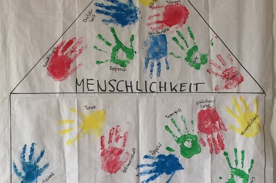 Bunte Handabdr&uuml;cke auf einem wei&szlig;en Blatt bilden ein Wertehaus mit den Begriffen Menschlichkeit, Familie, Erfolg und Zufriedenheit.