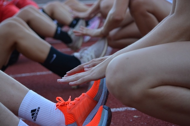 Gruppen von Sportlern dehnen auf einem Laufbahn, Fokus auf H&auml;nde und F&uuml;&szlig;e mit leuchtend orangen Schuhen.