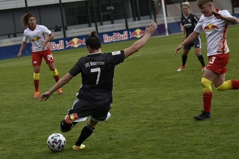 Zwei Fu&szlig;ballspielerinnen im Wettkampf, w&auml;hrend eine Spielerin einen Schuss auf den Ball ausf&uuml;hrt.