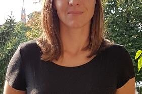 Portr&auml;t einer Frau mit schulterlangen Haaren, die in einem schwarzen Shirt vor einer gr&uuml;nen Gartenlandschaft steht.