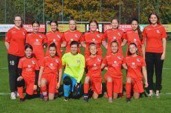 Mannschaftsfoto einer Frauenfu&szlig;ballmannschaft in roten Trikots, auf einem Sportplatz, im Hintergrund B&auml;ume.