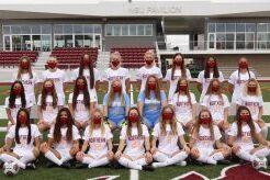 Gruppenfoto einer Fu&szlig;ballmannschaft in wei&szlig;en Trikots auf einem Sportplatz, mit Masken &uuml;ber den Gesichtern.
