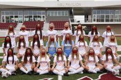 Gruppenfoto einer Fu&szlig;ballmannschaft in wei&szlig;en Trikots auf einem Sportplatz, mit Masken &uuml;ber den Gesichtern.