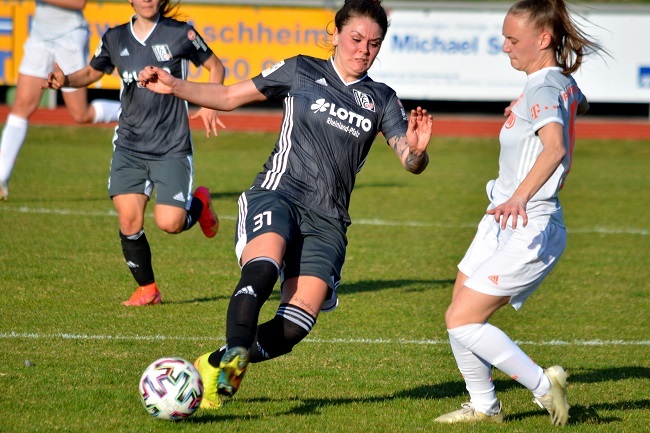Zwei Fu&szlig;ballspielerinnen im Wettkampf auf einem Rasenplatz, eine Spielerin setzt zum Schuss an.