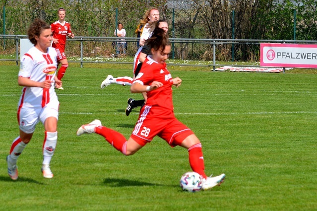 Zwei Fu&szlig;ballspielerinnen auf dem Platz, eine in rotem, die andere in wei&szlig;em Trikot, sprinten Richtung Ball.