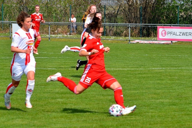 Zwei Fu&szlig;ballspielerinnen auf dem Platz, eine in rotem, die andere in wei&szlig;em Trikot, sprinten Richtung Ball.