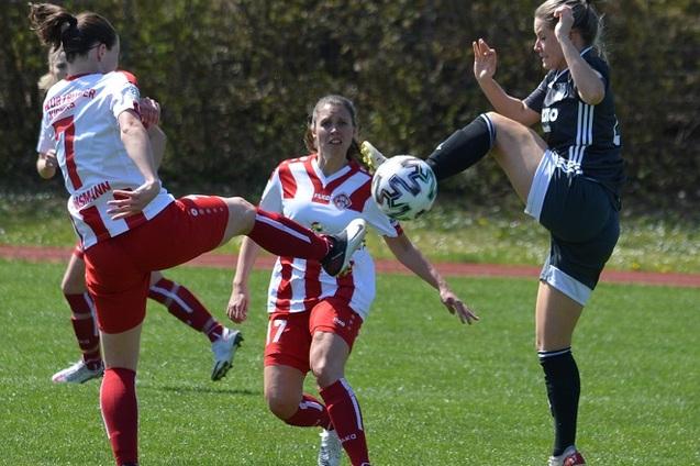 Frauenfu&szlig;ballspiel: Spielerinnen in roten und schwarzen Trikots k&auml;mpfen um den Ball auf einem gr&uuml;nen Rasenplatz.