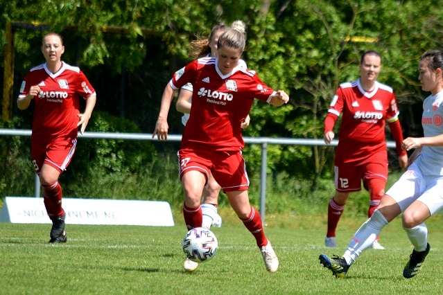 Spielende Frauenfu&szlig;ballerinnen in roten Trikots auf einem Rasenplatz, eine Spielerin schie&szlig;t auf den Ball.