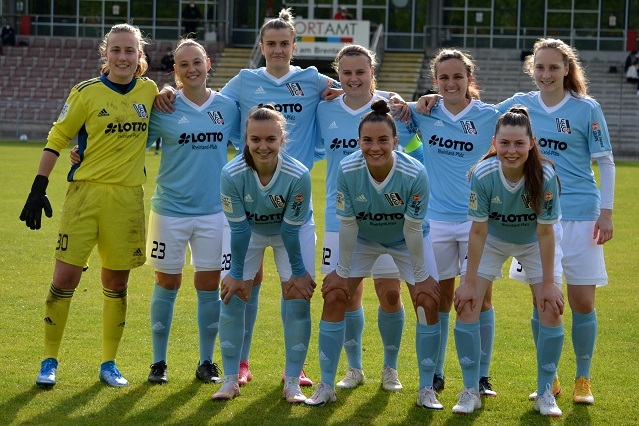 Mannschaftsportr&auml;t von neun Fu&szlig;ballspielerinnen in blauen Trikots auf einem Fu&szlig;ballplatz.