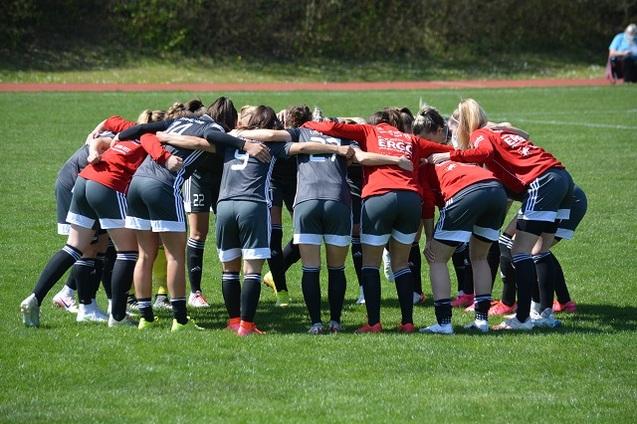 M&auml;dchenfu&szlig;ballmannschaft steht in einer huddle, tr&auml;gt rote und schwarze Trikots auf gr&uuml;nem Rasenfeld.