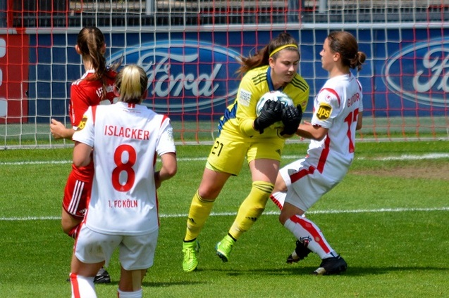 Torh&uuml;terin in gelbem Trikot f&auml;ngt den Ball vor zwei gegnerischen Spielerinnen auf dem Fu&szlig;ballfeld.