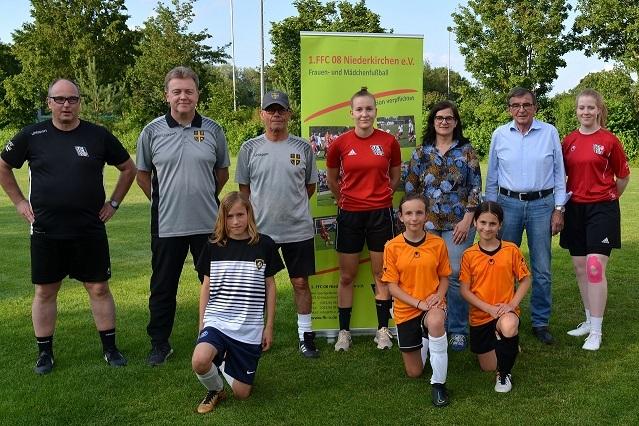 Gruppenbild mit Trainern und Spielerinnen des 1. FFC 08 Niederkirchen auf einem Fußballfeld vor einem Vereinsschild.