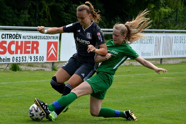 Zwei Fu&szlig;ballspielerinnen k&auml;mpfen um den Ball auf einem gr&uuml;nen Spielfeld w&auml;hrend eines Spiels.