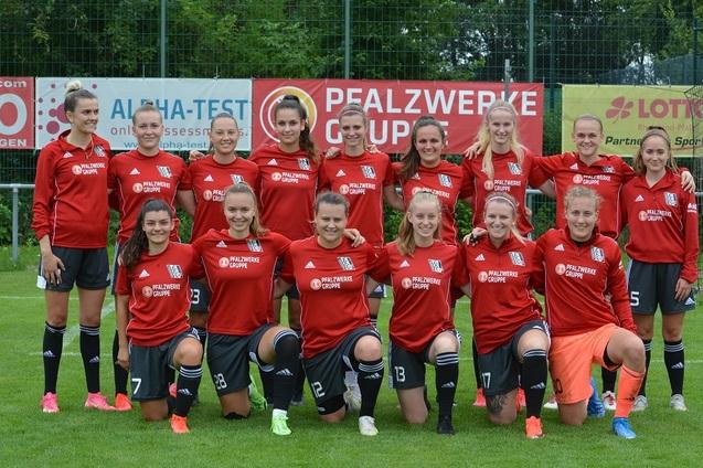 Gruppenshot eines Frauenfu&szlig;ballteams in roten Trikots mit schwarzen Hosen auf einem Sportplatz.