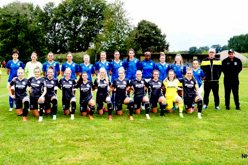 Gruppenschnappschuss einer Frauenfu&szlig;ballmannschaft auf einem gr&uuml;nen Spielfeld, ausgestattet mit Trikots in Schwarz und Blau.