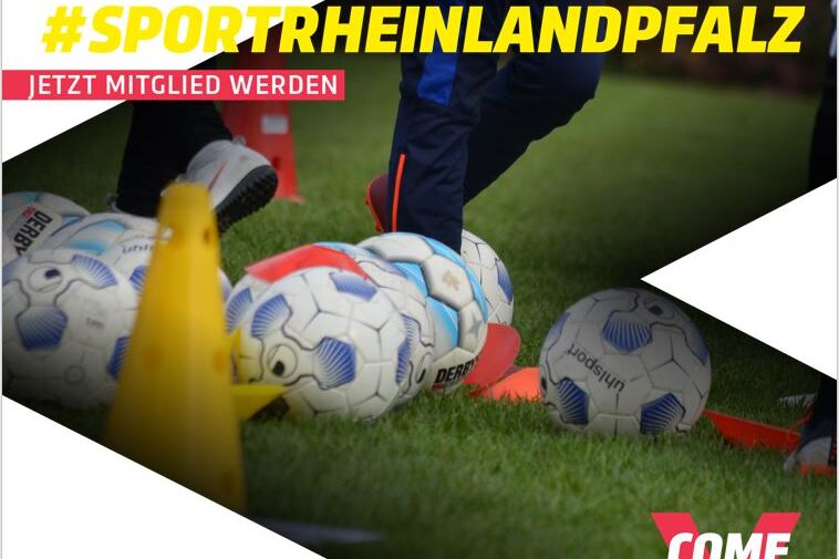 Fu&szlig;ball mit Trainingsmaterialien auf einem Sportplatz, Fu&szlig; eines Spielers mit blauem Hosenanzug im Hintergrund.