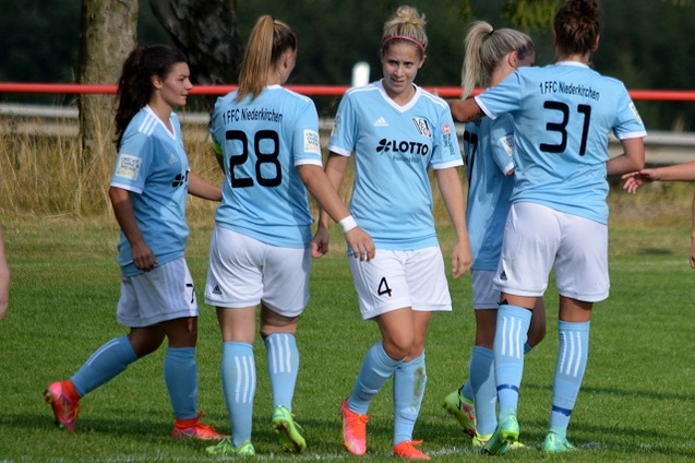 Frauenfu&szlig;ballmannschaft in blauen Trikots auf dem Platz, Spielerinnen zeigen Zusammenhalt und kommunizieren.