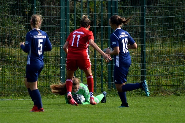 Spielszene mit einer Torh&uuml;terin, die einen Ball h&auml;lt, w&auml;hrend Spielerinnen in roten und blauen Trikots angreifen.