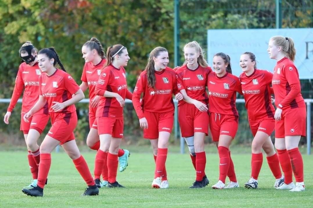 Eine Gruppe junger Fu&szlig;ballspielerinnen in roten Trikots feiert zusammen auf dem Feld.