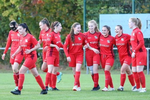 Eine Gruppe junger Fu&szlig;ballspielerinnen in roten Trikots feiert zusammen auf dem Feld.
