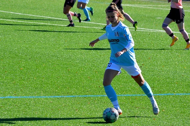 Fu&szlig;ballspielerin in blauen Trikots dribbelt den Ball auf einem gr&uuml;nen Kunstrasenplatz.
