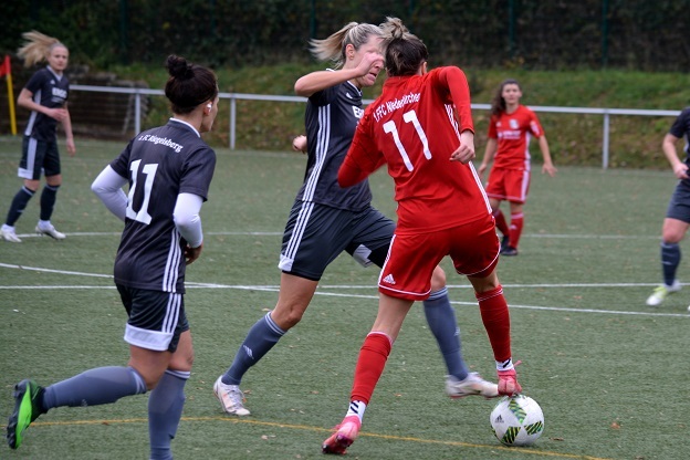 Zwei Frauenfu&szlig;ballspielerinnen in action, eine in rot, eine in grau, duelieren um den Ball auf einem Kunstrasenplatz.