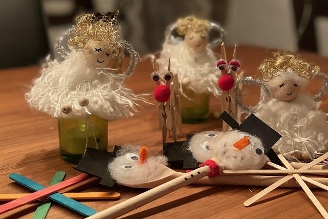 Bastelmaterialien und Figuren, darunter Engel und Schneemänner, auf einem Holztisch angeordnet.