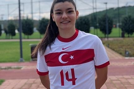 Junge Frau in Fu&szlig;balltrikot der T&uuml;rkei mit der Nummer 14, steht l&auml;chelnd auf einem Sportplatz.