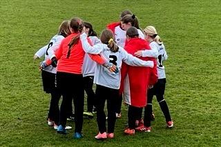 M&auml;dchenmannschaft bildet einen Kreis auf dem Fu&szlig;ballfeld vor dem Spiel, einige Spieler in roten und wei&szlig;en Trikots.