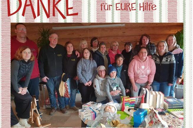 Gruppenshot von 20 Menschen in einem Raum, umgeben von Geschenken und einem Banner mit der Aufschrift &bdquo;DANKE f&uuml;r EURE Hilfe&ldquo;.