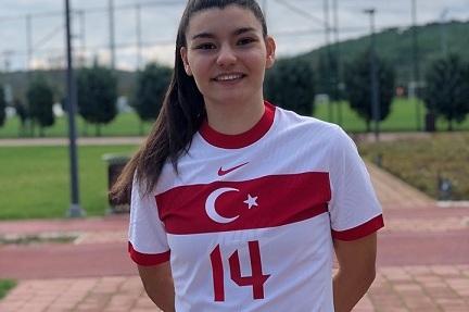 Junge Frau in Fu&szlig;balltrikot der T&uuml;rkei mit der Nummer 14, steht l&auml;chelnd auf einem Sportplatz.