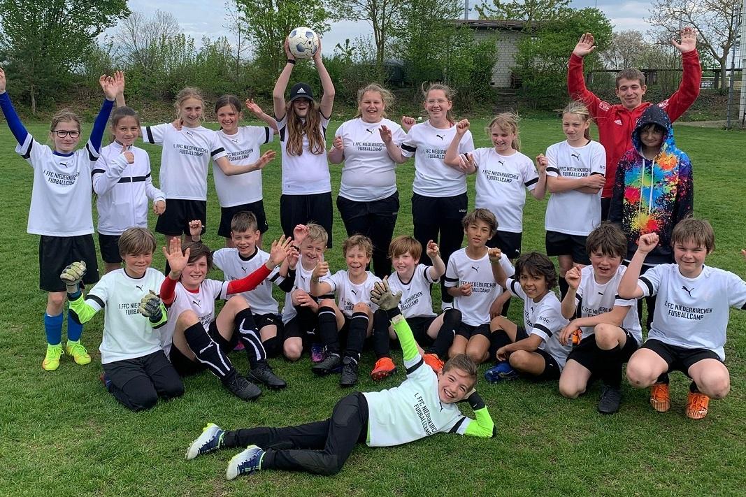 Gruppe von Jugendlichen in wei&szlig;en T-Shirts jubelt auf einem Fu&szlig;ballfeld, einige halten einen Ball in der Luft.