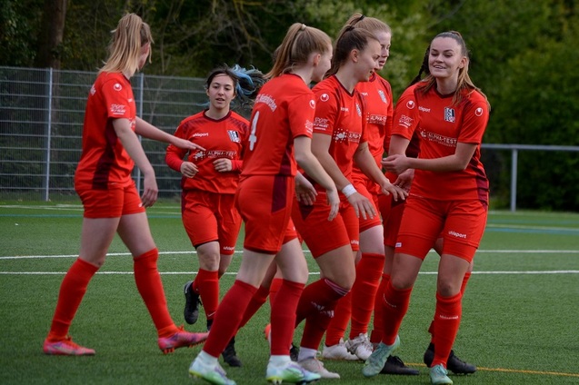 Gruppe junger Fu&szlig;ballspielerinnen in roten Trikots feiert gemeinsam auf einem Kunstrasenplatz.