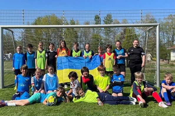 Gruppenszene von Jugendlichen mit Trikots, die vor einem Fu&szlig;balltor mit einer ukrainischen Flagge posieren.