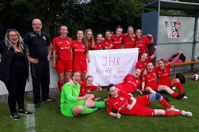 Mannschaft von Frauenfu&szlig;ballspielerinnen in roten Trikots posiert mit Banner nach einem Spiel am Fu&szlig;ballplatz.