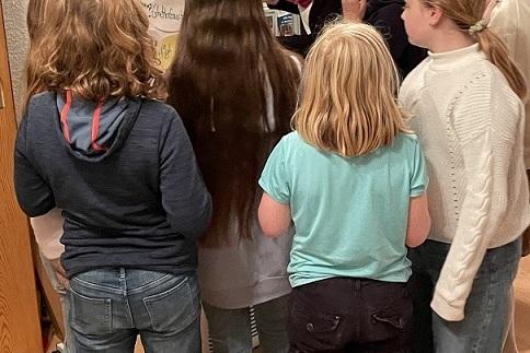 Gruppe von Kindern um einen Tisch versammelt, betrachtet ein Plakat mit dem Titel &bdquo;sch&ouml;ne Berufe&ldquo;.