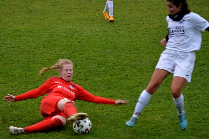 Zwei Fu&szlig;ballspielerinnen im Wettkampf, eine in roter, die andere in wei&szlig;er Kleidung, auf einem gr&uuml;nen Rasenplatz.