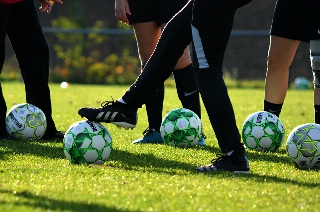 Gruppenspiel auf einem Rasenplatz mit mehreren Fu&szlig;ballen und Spielern in Sportkleidung.