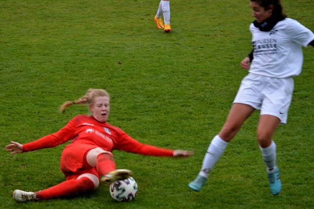 Zwei Fu&szlig;ballspielerinnen im Wettkampf, eine in roter, die andere in wei&szlig;er Kleidung, auf einem gr&uuml;nen Rasenplatz.